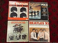 Four Beatles album covers laid out on a carpet showing front cover artwork and titles for 'A Hard Day's Night,' 'Something New,' 'Beatles VI,' and 'Beatles 65'.