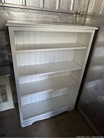 Front view of the white four shelf solid wood bookshelf showing shelf spacing and paneled back.