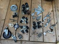 Overview of various clamps, caster wheels, and metal pulleys laid out on wooden surface showing quantity and styles.