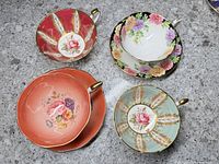 Overview of four cups and saucers showing floral designs, gold trim, and various color backgrounds.