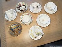 Overhead view of all 8 cup and saucer sets arranged on a wooden table showing various floral patterns and gold trim