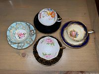 Top view of all four cups and saucers arranged in a square on wooden surface showing colors and patterns.