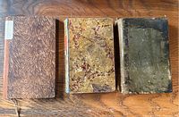 Photo showing three early 19th century German books with distinct old covers placed side by side on a wooden surface.