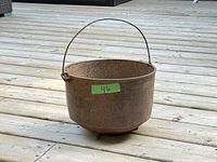 Early cast iron pot with rust on surface sitting upright with handle extended