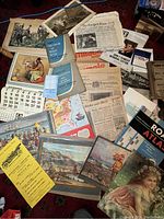 Photo showing a collection of vintage ephemera items spread on a carpet including manuals, newspapers, prints, and calendars