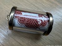 Close-up of the gold charm showing the rolled 10 Shilling note inside, visible through a transparent enclosure with gold bands on edges.