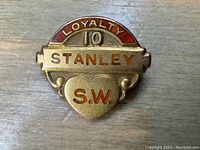 Front view of a small gold and red enamel Stanley 10 Year Loyalty pin with initials S.W. visible on heart-shaped section