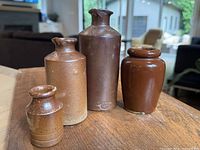 Four different sized redware and earthenware ink bottles displayed on wooden surface in natural and indoor lighting