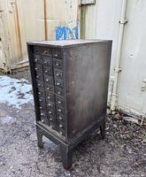 Left-front angle full view of metal cabinet outdoors on gravel