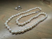 Full view of the pearl necklace laid flat along with matching pearl earrings, showing size and general condition.