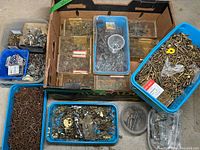 Multiple plastic bins containing a mixed assortment of brass screws, finishing nails, and other small metal fasteners