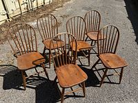 Six pine Windsor-style chairs grouped on asphalt surface, front view