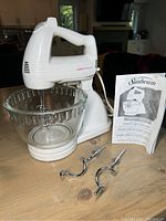 Full view of Sunbeam Mixmaster Model 2372 stand mixer with glass bowl, two pairs of beaters in front, and instruction manual upright.