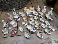 Overall view of all vintage McMaster pottery pieces grouped on wooden floor, showing multiple small planters and vases decorated with floral motifs.