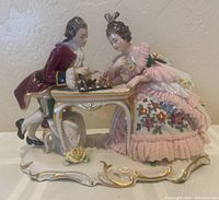 Front view of the porcelain figurine showing the couple playing chess with fine details on clothing and chessboard.