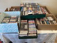 Photo showing multiple boxes and trays filled with music cassette tapes, showcasing the large quantity and diversity of the collection.