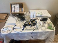 Full overview of the Nintendo Wii bundle showing console, controllers, steering wheels, Wii Fit balance board, game discs, cables, and accessories arranged on a table.