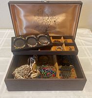 Open brown cloth jewelry box showing various compartments with assorted jewelry and small picture frame insert on top.