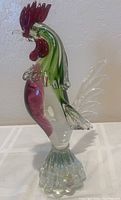Side profile of the Murano glass rooster showing red comb, green body, clear tail and pedestal base.