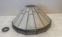 Front and side angle view of a Tiffany style lamp shade with a steel screw piece beside it. The shade has white and green stained glass panels with a geometric design.