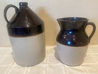 Front view of two vintage crocks, taller jug on left and smaller pitcher on right, showing color and size.