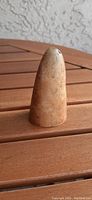 Photo of the artifact standing upright on a wooden surface, showing rounded top and beige texture with some natural marks.