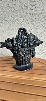 Front view of the black cast iron fruit basket doorstop on a wooden table against a stucco wall.