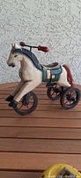 Side view of wooden horse tricycle toy showing painted details and structure with four wheels and handlebar