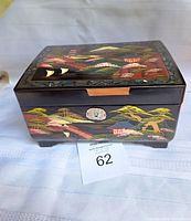Front view of the vintage black lacquer music box showing detailed hand painted Japanese landscape scene and decorative lock plate.