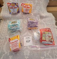 Photo of six McDonald's promotional toys sealed in original packaging, laid out on bedding.
