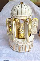 Porcelain carillon church with four open doors showing angel figure inside, off-white and gold tone with dome top