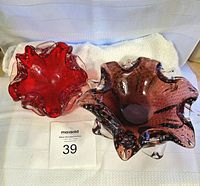 Two biomorphic glass bowls, one ruby red and one amethyst, shown top down on white textured cloth.