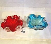 Two art glass bowls side by side, one ruby red and one aqua blue with biomorphic shapes and ruffled edges.