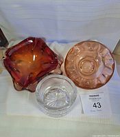 Three vintage glass ashtrays shown together: clear crystal round, square red amber Murano sommerso, and large pink glass ashtray.