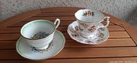 Photo displaying the two Royal Albert teacups with matching saucers on a wooden surface, showing floral patterns and gold trims.