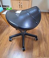 Front side view of black saddle chair showing seat shape and five-wheeled base.