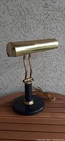 Front view of vintage brass bankers lamp showing its cylindrical shade, brass rods, and marble base.