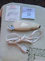 Cream-colored Cameo electric scissors with pointed blade and white power cord, placed on fabric surface beside instruction manual and auction tag.
