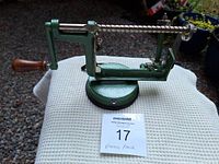 Vintage metal peeler with green finish and suction cup base on a white cloth with outdoor background