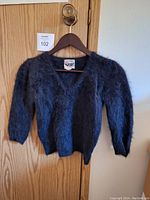 Front view of vintage angora sweater on hanger showing fuzzy thick knit fabric, V-neck, and 3/4 sleeves.