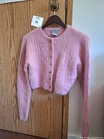 Front view of a pink angora wool sweater on a hanger, showing button-up front with round neckline, long sleeves, and tapered waist.