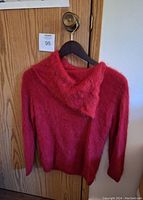 Front view of thick knit red angora wool sweater with cowl-neck on black hanger against wooden door.