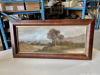 Frontal view of the framed pastel landscape showing fall country scene with trees, house, hills under cloudy sky in a wooden frame.