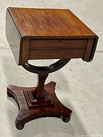 Front angle view of antique parlour table showing solid wood top, drawers with keyholes, and bowed center support with base on caster wheels.