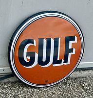Photo of the circular orange Gulf metal wall button showing the full logo and edge detail.