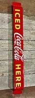 Full front view of red Coca Cola porcelain push bar with bright yellow and white lettering on wooden background.