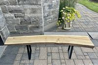 Full view of the live edge solid cedar wood bench showing the wood grain and black metal legs on a stone patio.