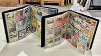 Two open black binders displaying multiple pages of Pokemon trading cards in plastic sleeves arranged in rows of nine cards per page.
