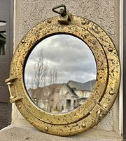 Front view showing tarnished brass porthole frame with clear round mirror reflecting outdoor scene.