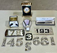 Overview of vintage lot including Onyx mantel clock, Parker 61 pen with box, metal house numbers, and stained glass pieces all displayed on a table.
